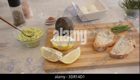 Preparing wooden cutting board with whole avocado, halved lemon, bread slices on marble countertop Stock Photo
