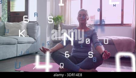 Meditating senior woman wearing gray top on pink mat in living room with floating code symbols Stock Photo