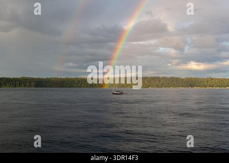 Campbell River, BC  Canada - 23 JUN 2024: Sailboat in Discovery Passage beneath a double rainbow and a mostly cloudy sky. Stock Photo