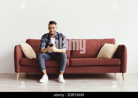 Man Sitting on a Red Couch Using a Smartphone in a Modern Indoor Space During the Day Stock Photo