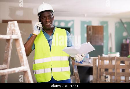 African american foreman with documents in his hands is talking on a mobile phone Stock Photo