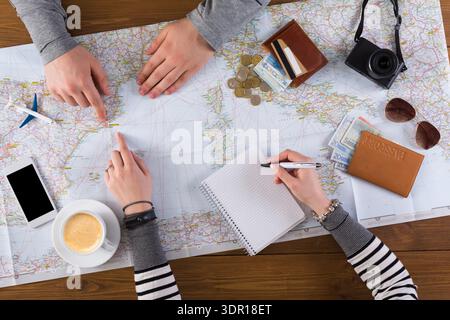 Friends Planning a Road Trip Using a Map at a Table With Coffee and Travel Supplies Stock Photo