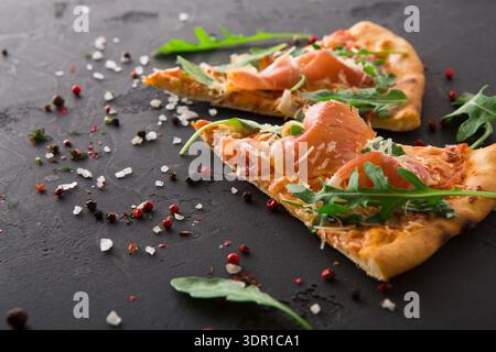 Slices of Pizza Topped With Smoked Salmon and Arugula on a Dark Surface Stock Photo
