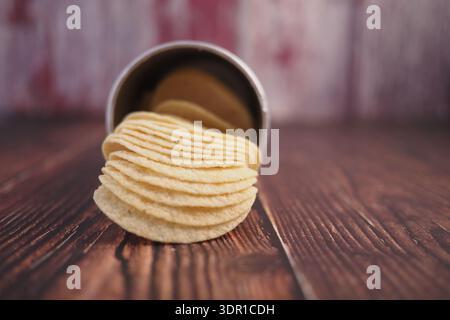 Crispy potato chips spill from a can on wooden table Stock Photo
