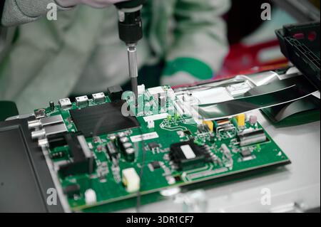 Workers assemble a circuit board at a television manufacturing plant focusing on precision and quality control Stock Photo