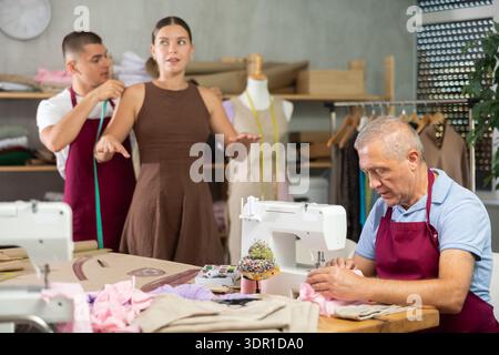 Tailor takes measurements from a woman next to an elderly employee of the atelier Stock Photo