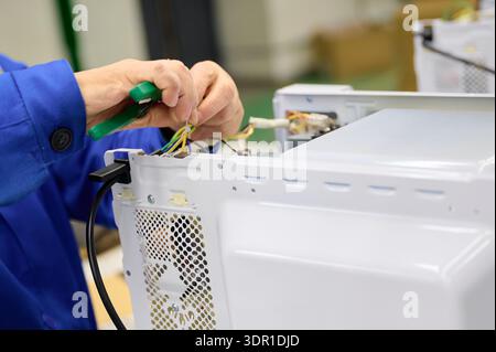 Assembly of electrical components for microwave ovens on a conveyor belt in a manufacturing facility Stock Photo
