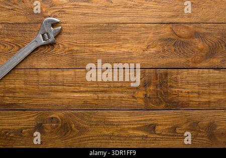 A Metal Adjustable Wrench Rests on a Wooden Surface in a Well-Lit Workspace During the Day Stock Photo