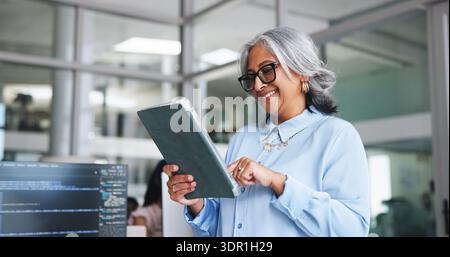 Smile, woman and tablet for programming in office for research, software manual and coding. Mature person, digital app and troubleshooting for website Stock Photo