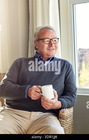 Coffee, cozy and thinking with old man in living room of home for peace, reflection or wellness. Ideas, memories and smile with senior person drinking Stock Photo