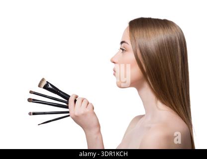 Woman Holds Makeup Brushes While Looking to the Side in a Studio Setting Stock Photo