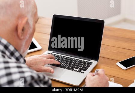 Senior Man Working on Laptop and Taking Notes at a Wooden Table During Daytime Stock Photo