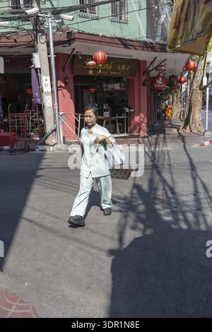Bangkok, Thailand. March 25th 2025. A local women walking past Chinese restaurants and the shadows of overhead electrical wires in the Chinatown distr Stock Photo