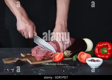 Chef Cuts Meat on a Wooden Board With Fresh Vegetables During Meal Preparation Stock Photo
