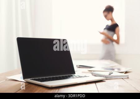 Woman Using Mobile Phone While Standing Next to Laptop on Wooden Table in Bright Room Stock Photo