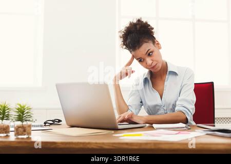 Woman Works on Laptop While Looking Thoughtful at Desk in Bright Office Space Stock Photo