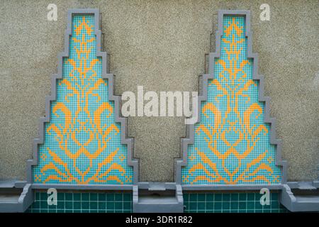 Symmetrical stepped triangular mosaic panels featuring blue and yellow geometric tile patterns on textured wall. Stock Photo