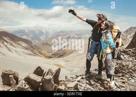 Happy couple of hikers taking selfie picture on top of the mountain - Two travelers with backpack smiling together at camera - Travel blogger influenc Stock Photo