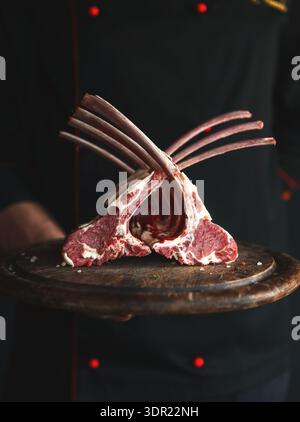 Collection of Raw Lamb Chops Displayed on a Wooden Plate by a Chef in a Dark Kitchen Setting Stock Photo
