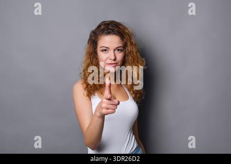 Woman Points Finger While Standing Against a Gray Wall in a Simple Setting Stock Photo