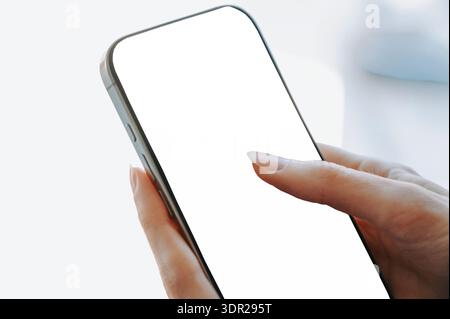 Close-up of a woman touching a blank white smartphone screen in soft natural light. Clean mockup with copy space, ideal for mobile app design, digital Stock Photo