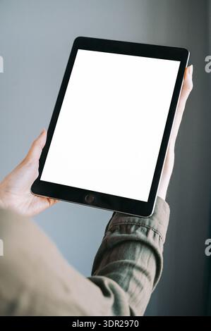 Close-up of hands holding a tablet with a blank white screen against a clean, neutral background. Ideal for app presentation, UI design showcase, digi Stock Photo