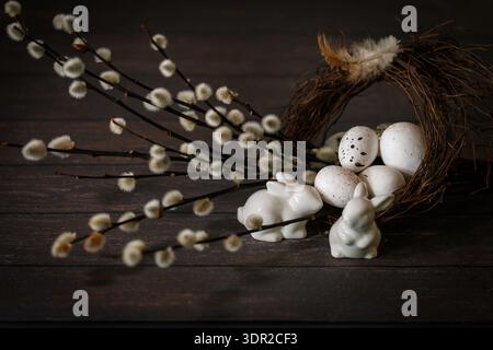 Happy Easter card with copy space. A festive composition with decorative eggs in a nest, willow twigs and ceramic figures of rabbits on a dark brown Stock Photo