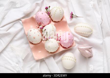 Ceramic holder, flowers, bunny and Easter eggs decorated with pearls on white fabric Stock Photo