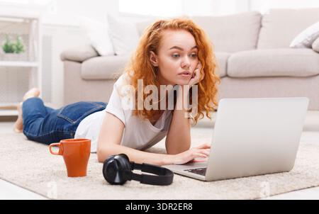 Young Woman Works on Laptop While Lying on Floor in Living Room During the Afternoon Stock Photo