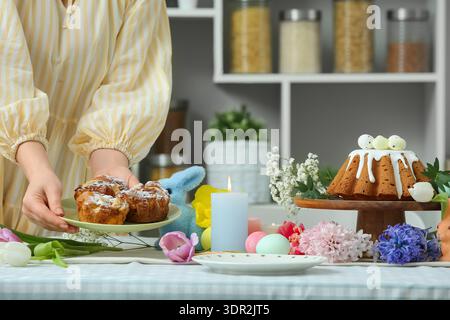 Woman putting Easter cake on table setting for Easter celebration in kitchen. Closeup Stock Photo