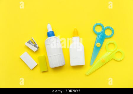Bottles of glue, scissors and stapler on yellow background. Top view Stock Photo