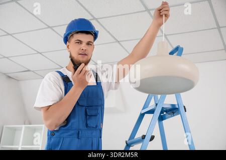 Male contractor talking on radio transmitter near hanging lamp in room Stock Photo