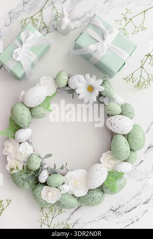 Composition with Easter wreath made of green painted eggs and bunny figurine and gifts on white table Stock Photo