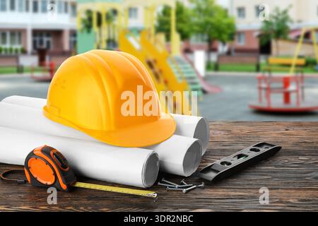 Hardhat, blueprints and construction supplies on wooden table at playground outdoors Stock Photo