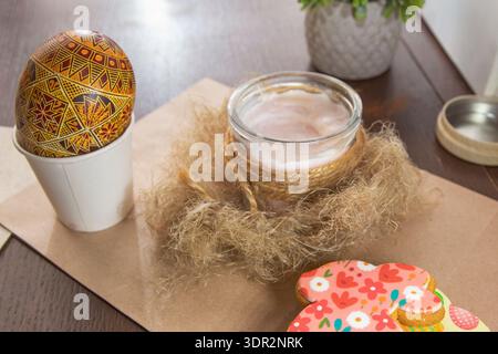 Decorated Ukrainian Easter egg with glass candle jar and festive cookies on wooden table Stock Photo