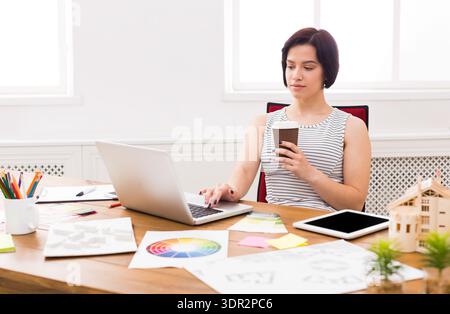 Woman Working at Desk With Laptop and Holding Coffee Cup During Day in Office Stock Photo