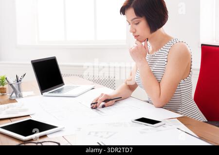 Woman Works on Design Sketches at a Desk With Technology in a Bright Room Stock Photo