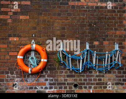 Orange lifebuoy and rope ladder on a brick wall Stock Photo