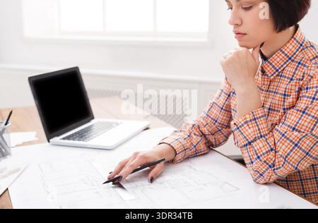 Woman Focuses on Drawing Plans at a Desk in a Bright Office Setting in the Morning Stock Photo