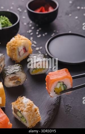 Collection of Sushi Rolls Served on a Dark Plate With Various Toppings and Condiments in Small Bowls Stock Photo
