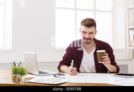 Man Sitting at Desk Working With Laptop and Coffee While Looking at Documents Stock Photo