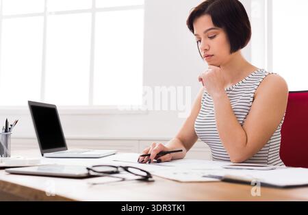 Woman Works at Desk With Laptop and Documents During Daytime in Bright Room Stock Photo