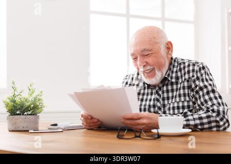 Senior Man Reading Documents With a Smile While Sitting at a Table in a Bright Room Stock Photo