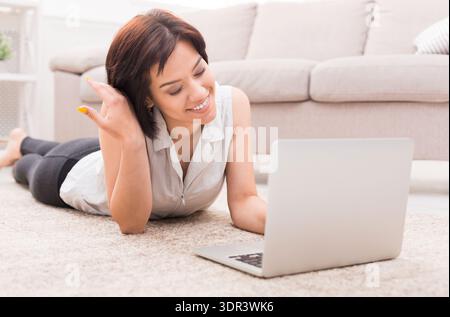 Woman Relaxes on Carpet While Connecting With Friends Online Using Laptop Stock Photo
