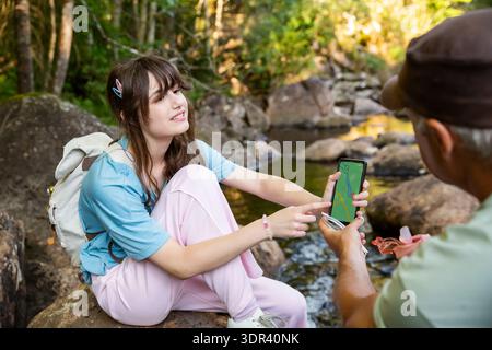 Family hikers using navigation app on smartphone in forest. Daughter showing map to father during trekking. Technology in nature and travel concept. Stock Photo