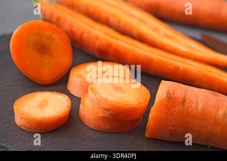 Fresh Carrots on a Dark Surface With Some Cut Into Round Slices for Cooking or Salad Stock Photo