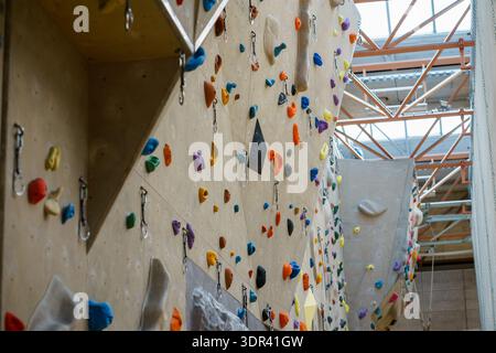 Indoor climbing wall with multicolored holds and safety anchors in a modern gym, designed for training, fitness, and recreational rock climbing. Stock Photo