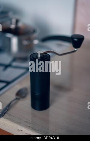 A compact manual coffee grinder sits on a countertop beside a stove pot Stock Photo