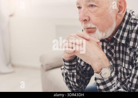Man Sits on Couch Indoors With Hands Clasped and Deep in Thought During the Afternoon Stock Photo