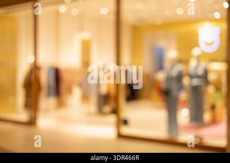 blurred view of a modern luxury fashion boutique storefront with warm golden lighting and elegant mannequins, creating a sophisticated shopping mall a Stock Photo